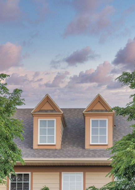 Vertical clouds at sunset Roof of a house with two gabled dormer windows at Utah. Roof exterior of a house with gray asphalt composite shingles and vinyl wood wall sidings with trees at the front. - Foto, afbeelding