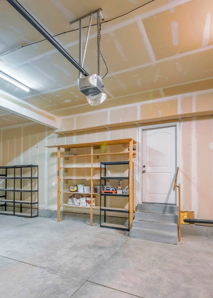 Vertical Large unfinished garage interior with wall patch marks. There are two automatic door operators on the ceiling and storage racks and shelving - Photo, Image