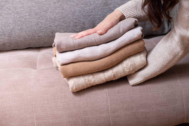 Stack of cozy knitted sweaters in female hands on sofa background. Warm concept. - Photo, Image