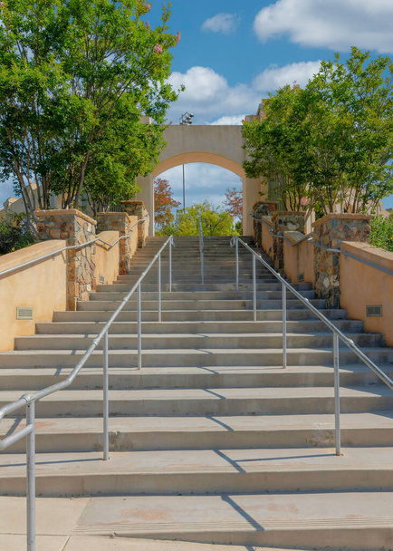 Vertical White puffy clouds Public park entrance with floor-mounted and wall-mounted handrails. Low angle view of a stairs with concrete steps and arched concrete entryway at the top in the middle of trees and plants. - Photo, Image