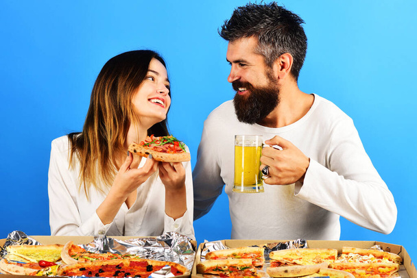 Счастливая пара, сидящая за столом, ест пиццу и пьет пиво, веселясь вместе. Доставка продуктов питания - Фото, изображение