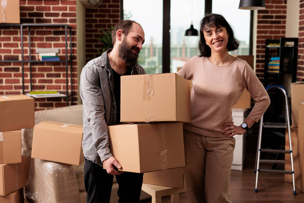 Portrait of caucasian couple carrying boxes to move in apartment property, using furniture storage to decorate family home. Enjoying household relocation to start new beginnings. - Foto, Imagen