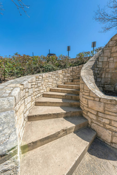 Outdoor staircase with stone walls and concrete steps at San Antonio, Texas. Curved staircase near the shrubs on the left against the view of sign posts and sky at the back. - Foto, imagen