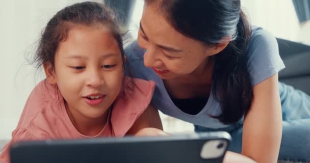 Маленька дівчинка-підліток з Азії з матір'ю грає на цифровому планшеті на підлозі килима, радіючи у вітальні вдома. Родина проводить разом час, творчий спосіб життя для дитячої концепції. - Кадри, відео