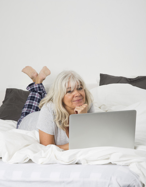 Женщина средних лет с ноутбуком в постели
 - Фото, изображение