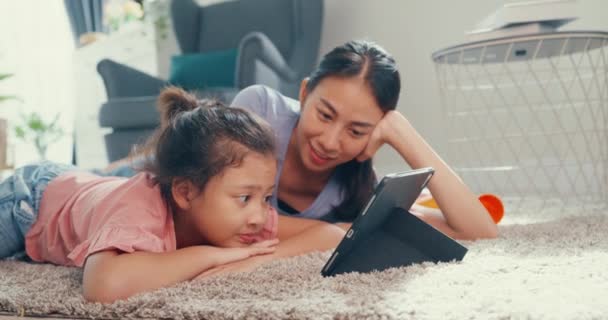 Маленька азіатська дівчинка з матір'ю дивиться цифрову табличку на підлозі килима, насолоджуючись приємним моментом у вітальні вдома. Родина проводить разом час, творчий спосіб життя для дитячої концепції. - Кадри, відео