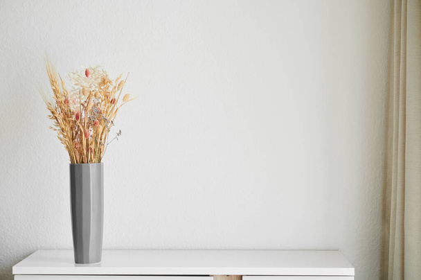 Beautiful dried flowers in a gray vase, against the background of a white wall in the interior. Wheat in a vase. - Foto, immagini