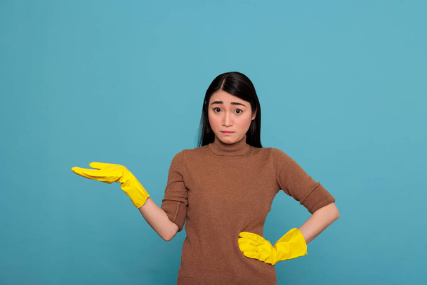 Ασιάτισσα γυναίκα με τρομακτική έκφραση προσώπου δείχνοντας το χέρι στην άκρη στο χώρο αντιγραφής και φορώντας κίτρινα γάντια για την ασφάλεια, οικιακή εργάτης, Καθαρισμός έννοια σπίτι, τόνισε ανησυχούν θηλυκό - Φωτογραφία, εικόνα