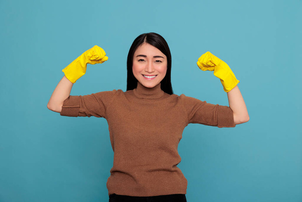 Happy energetic beautiful asian housewife raising arms and showing biceps isolated blue background, Housewife worker, Cleaning home concept, Female smiling after completing his job, - Zdjęcie, obraz