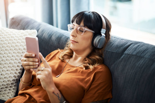 The right music will leave you feel soothed. a young woman wearing headphones while using her cellphone at home - Foto, Bild