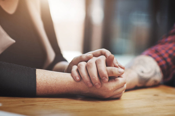 Support, compassion and trust while holding hands and sitting together at a table. Closeup of a loving, caring and affectionate couple comforting and helping each other through a difficult time. - Фото, изображение