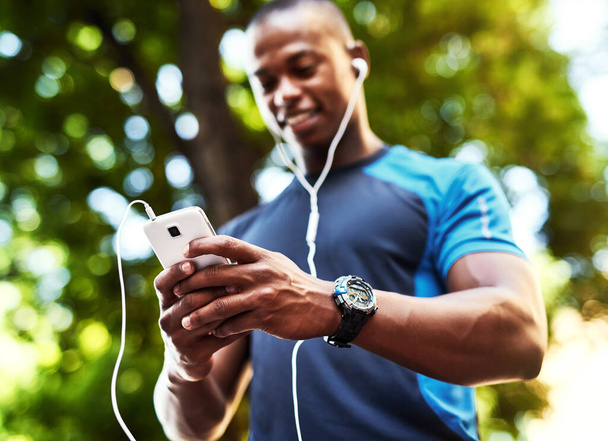 This is what I call connection on the go. a handsome young man listening to music and using his cellphone while exercising outdoors in the city - Photo, Image