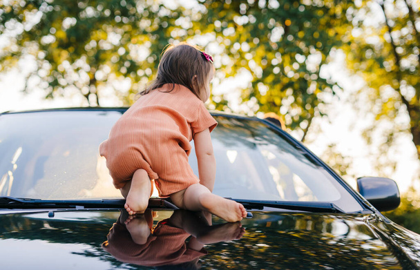 Baby girl crawling on car bonnet. Summer nature. Happy family, childhood. Road trip. - Photo, image