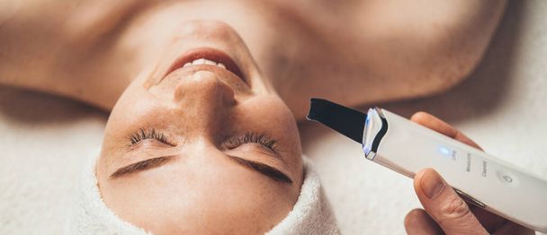 Close-up portrait of smiling woman receiving ultrasound cavitation facial peeling. Skin treatment. Facial beauty. Healthy lifestyle. Skin care. Professional - Fotó, kép