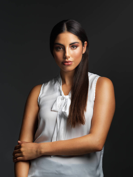 Modesty is beautiful. Portrait of an attractive young woman wearing a white blouse and posing alone against a dark background in the studio - Photo, Image