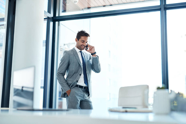 Да, мой бизнес процветает. бизнесмен разговаривает по мобильному телефону, стоя в своем офисе - Фото, изображение