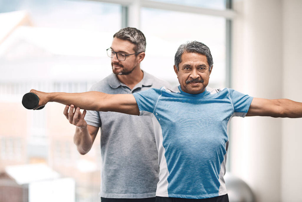 Exercise is vital in your senior years in life. a senior man exercising with dumbbells during a rehabilitation session with his physiotherapist - Photo, image