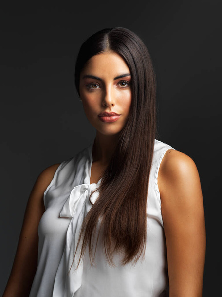 Staring straight into the face of challenges. Portrait of an attractive young woman wearing a white blouse and posing alone against a dark background in the studio - Foto, Imagem