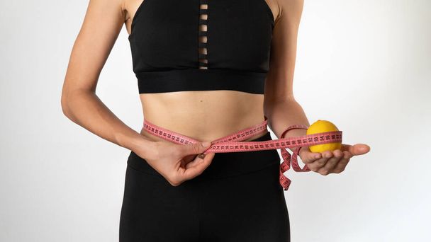 Eine Frau misst die Figur mit einer Schleife, einer Zitrone in der Hand - Gewichtsverlust, gesunde Ernährung und Sport. Hochwertiges Foto - Foto, Bild