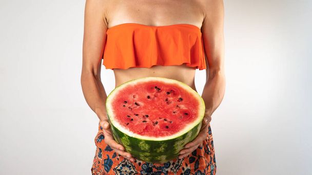 Woman in bathing suit - orange shorts and top with half a watermelon in her hands - summer wave. High quality photo - Fotografie, Obrázek