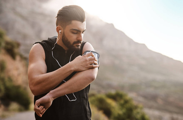 Got to first put some music on. a sporty young man listening to music while exercising outdoors - Foto, Bild