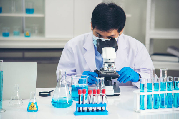 Bilim adamı bilim laboratuarındaki mikroskop araştırmalarını inceliyor. Asyalı bilim adamı laboratuvar kimya laboratuvarlarını arıyor. Covid-19 Coronavirus biyokimya araştırma deneyi aşı konsepti - Fotoğraf, Görsel