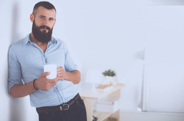 Young man standing near wall and holding cup of coffee. - Φωτογραφία, εικόνα