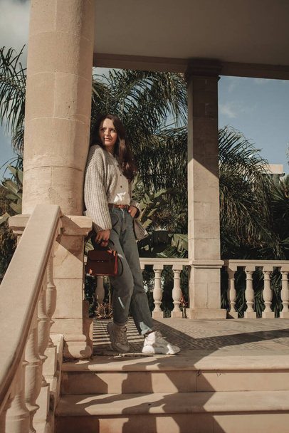 Młoda kobieta stoi i cieszy się w pobliżu starego budynku z kolumnami i tropikalnych roślin w Larnaca, Cypr. - Zdjęcie, obraz