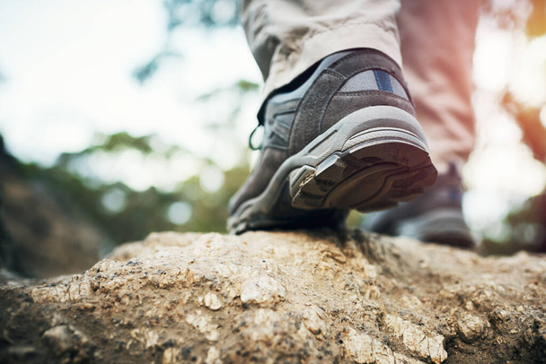 Χρειάζεται μόνο ένα βήμα. Χαμηλή γωνία βολής ενός αγνώριστου άνδρα που περπατάει σε βράχους έξω από ένα βουνό κατά τη διάρκεια της ημέρας - Φωτογραφία, εικόνα