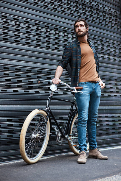 Modern day men roll around in these type of wheels. Full length shot of a handsome young man posing next to his bicycle outdoors - Фото, изображение