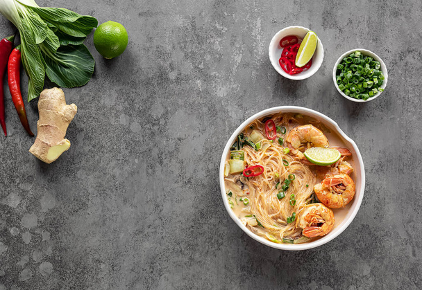 Laksa Shrimp bowl. glass noodle dish, top view, copy space. Asian Malaysian food with shrimps, bok choy, lime, ginger, and chili. Most variations of laksa are prepared with spicy coconut soup. - Fotoğraf, Görsel