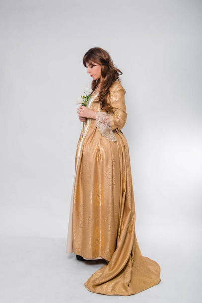 Full length portrait of a woman in a gold dress in the style of the rococo era, standing and posing with a flower in hand isolated on a white background. - Photo, image