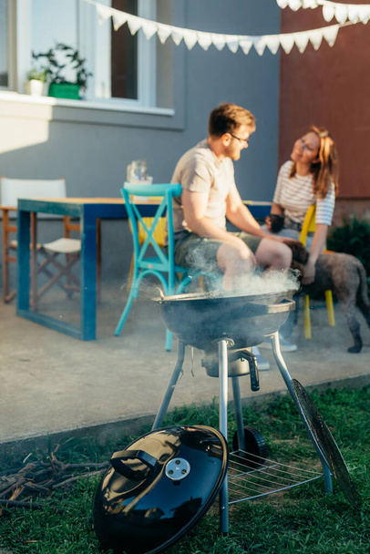 close up of barbecue smoking. couple with dog in blurred background - Photo, Image