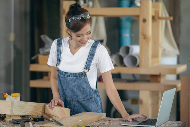 A carpenter woman works in her own woodworking shop. She uses a tablet while in her workspace. small business concept - Foto, afbeelding