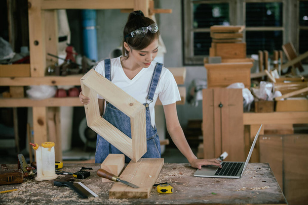 Professional carpenter. A woman works in a carpentry shop using a tablet to design furniture in a wood shop. - 写真・画像