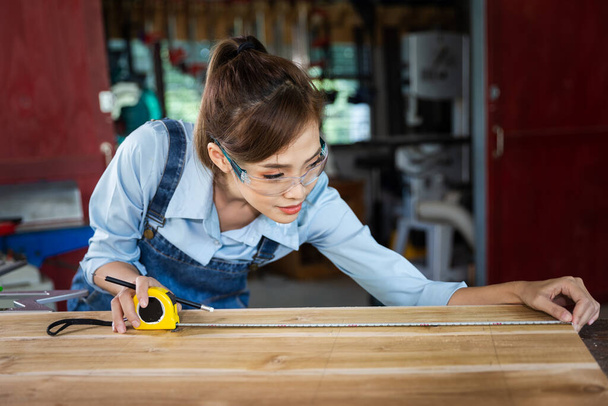 χαρούμενη ελκυστική σκληρά εργαζόμενη μεσήλικη επαγγελματίας ξυλουργός που ψάχνει και επιλέγει ξύλο στο εργαστήριο. - Φωτογραφία, εικόνα
