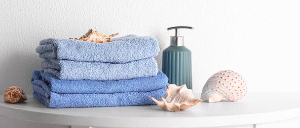 Stack of clean towels, sea shells and soap on table in bathroom - Photo, Image