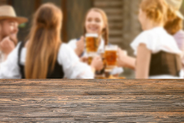 Empty wooden table and happy people with beer celebrating Octoberfest outdoors. Mockup for design - Fotografie, Obrázek