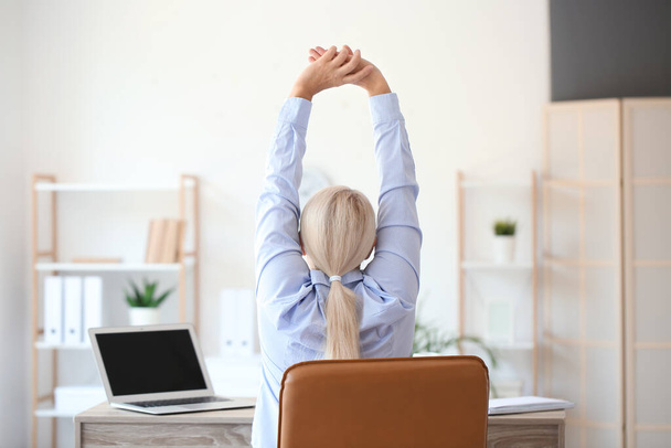 Зрелая деловая женщина с болью в спине делает упражнения в офисе - Фото, изображение