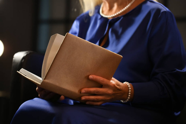Mature woman reading old book at home late in evening, closeup - Фото, зображення