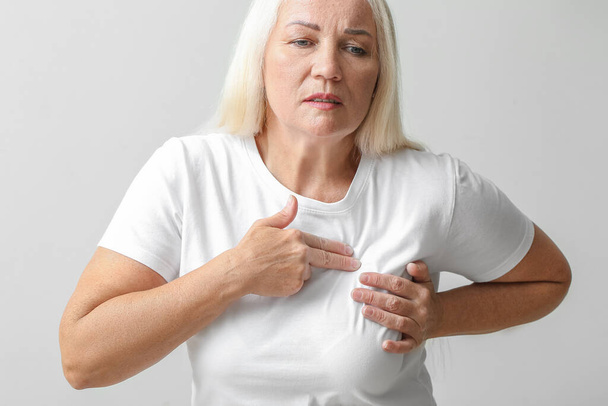 Mature woman suffering from breast pain on light background - Valokuva, kuva