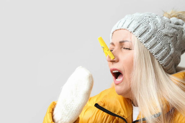 Ill mature woman with clothespin on light background. Stuffy nose concept - Foto, Imagen