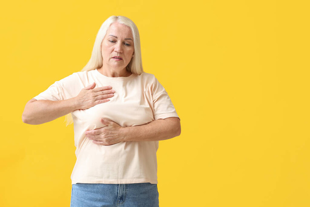 Mature woman suffering from breast pain on yellow background - Photo, image