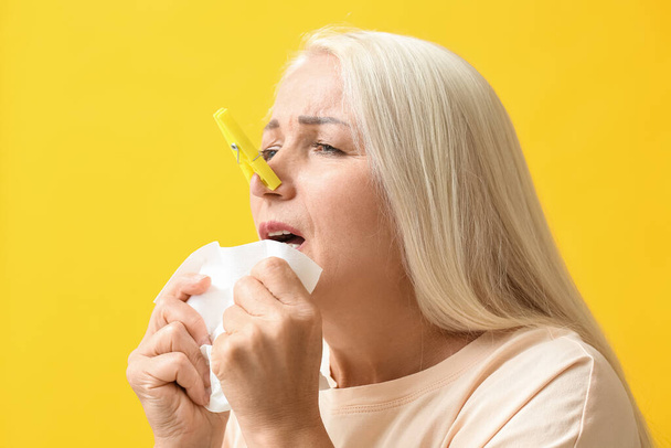 Ill mature woman with clothespin and tissue on yellow background. Stuffy nose concept - Foto, Bild