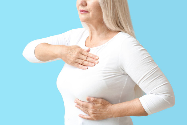 Mature woman suffering from breast pain on blue background - Foto, Imagem