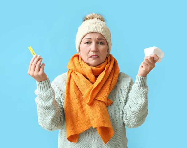Ill mature woman with clothespin and tissue on blue background. Stuffy nose concept - Foto, Imagem