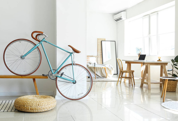 Современный велосипед на деревянной скамейке возле светлой стены в спальне - Фото, изображение