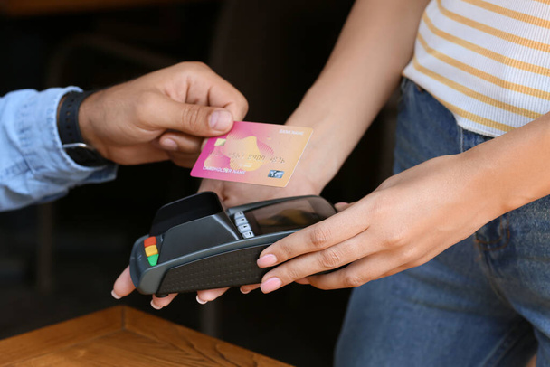 Человек, оплачивающий кредитной картой через платежный терминал за столом в кафе, крупным планом - Фото, изображение