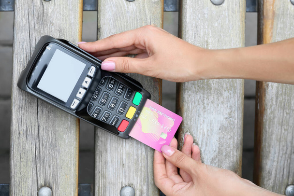 Woman paying with credit card via payment terminal on bench outdoors, closeup - Zdjęcie, obraz