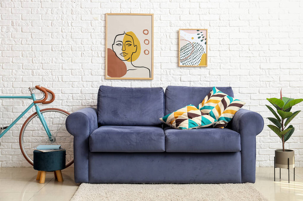Bicycle, blue sofa, pouf and houseplant near white brick wall - 写真・画像